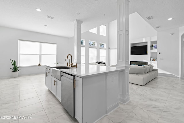 kitchen with dishwasher, a kitchen island with sink, visible vents, and decorative columns