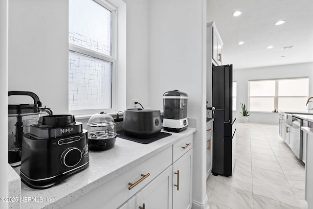 kitchen with recessed lighting, white cabinetry, stainless steel dishwasher, freestanding refrigerator, and light stone countertops