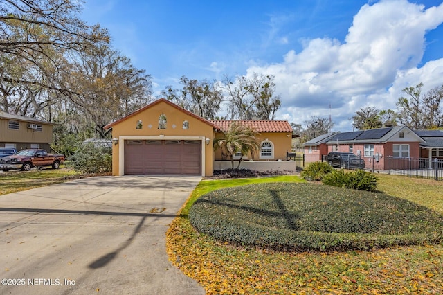 mediterranean / spanish-style house featuring driveway, a tiled roof, an attached garage, fence, and stucco siding