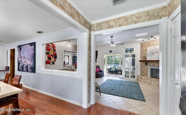 interior space with a textured ceiling, a stone fireplace, ornamental molding, and visible vents