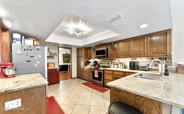 kitchen with visible vents, decorative backsplash, appliances with stainless steel finishes, a tray ceiling, and a sink