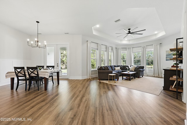 living room with visible vents, a tray ceiling, recessed lighting, ceiling fan with notable chandelier, and wood finished floors