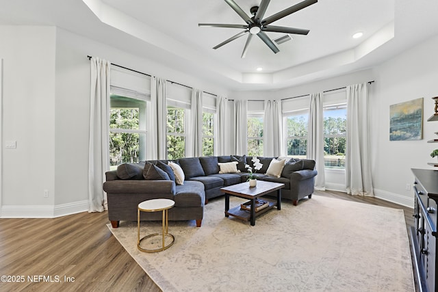 living area with a tray ceiling, recessed lighting, wood finished floors, and baseboards