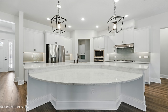 kitchen featuring a sink, under cabinet range hood, white cabinetry, stainless steel appliances, and a large island with sink