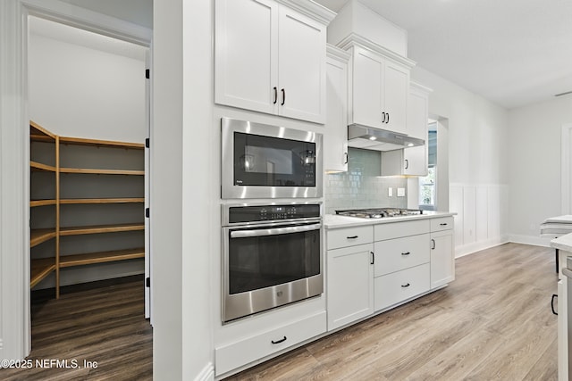 kitchen featuring under cabinet range hood, stainless steel appliances, light wood-type flooring, and light countertops