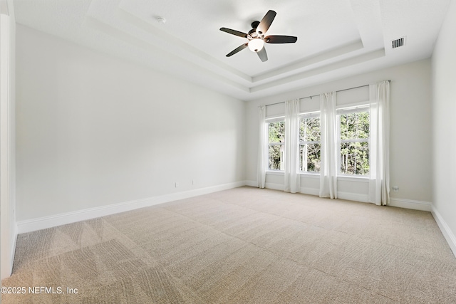 carpeted spare room with visible vents, baseboards, a tray ceiling, and a ceiling fan