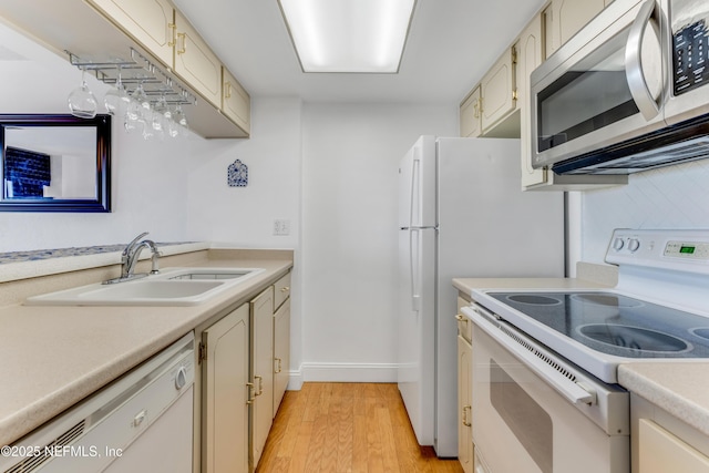 kitchen with white appliances, cream cabinets, light countertops, light wood-style floors, and a sink