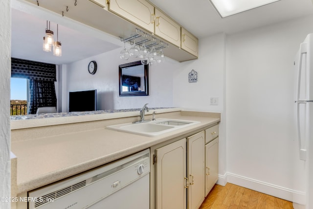 kitchen with white appliances, a sink, baseboards, light countertops, and light wood-type flooring