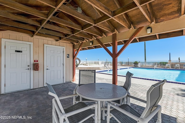 view of patio featuring outdoor dining area, fence, and a community pool