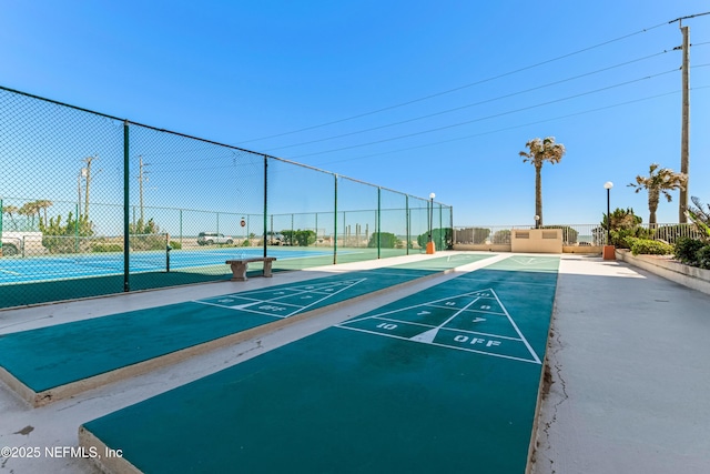 view of community with shuffleboard, fence, and a tennis court