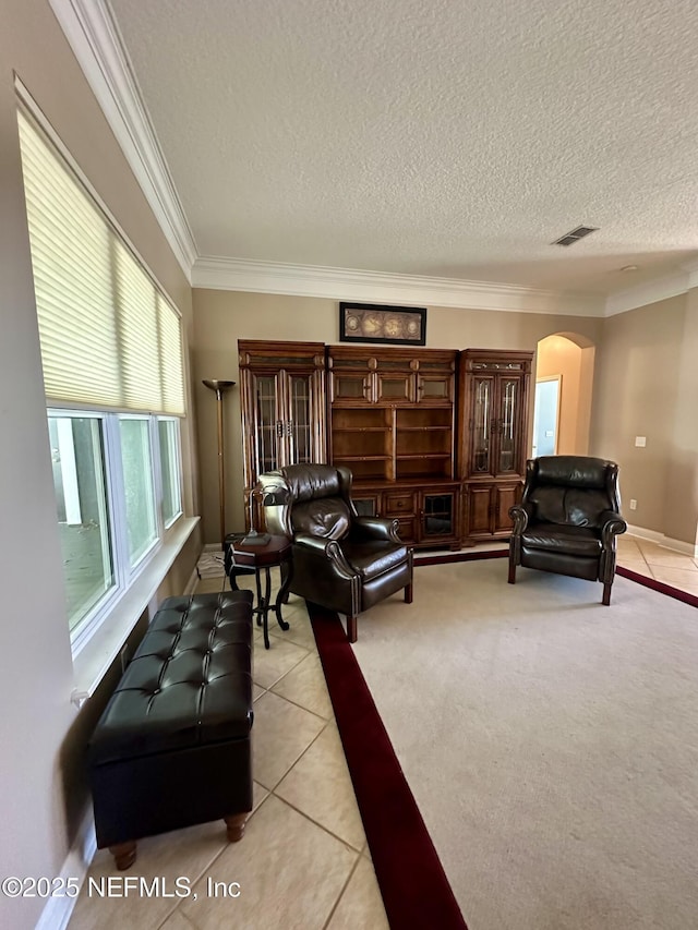 living room with arched walkways, a textured ceiling, light tile patterned flooring, visible vents, and ornamental molding