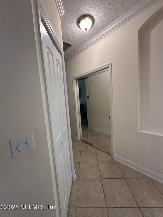 corridor featuring crown molding, visible vents, a textured ceiling, baseboards, and tile patterned floors