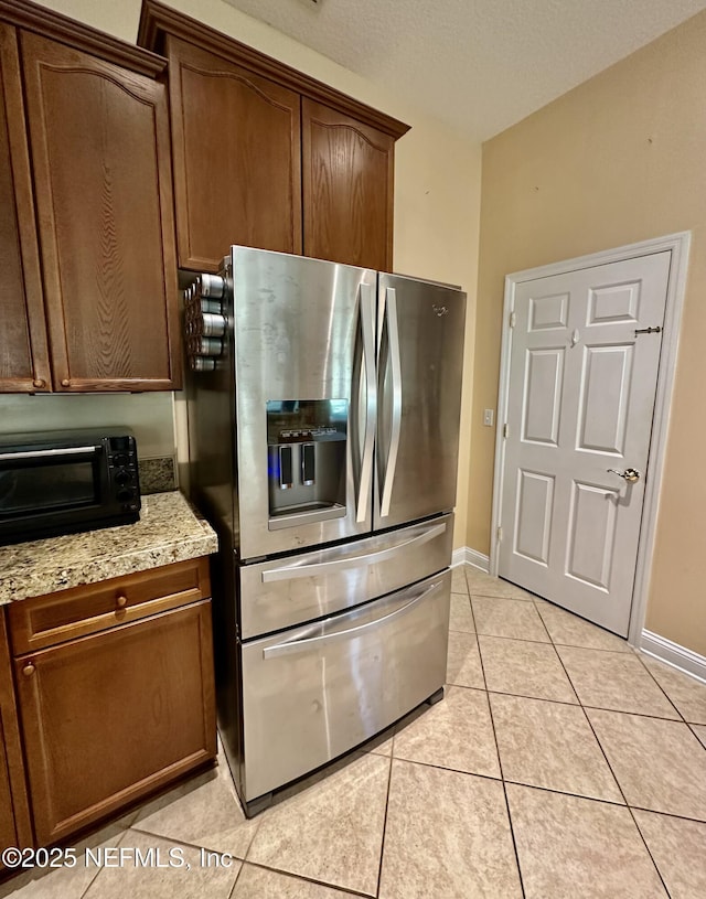 kitchen with light stone counters, a toaster, light tile patterned floors, stainless steel fridge, and baseboards