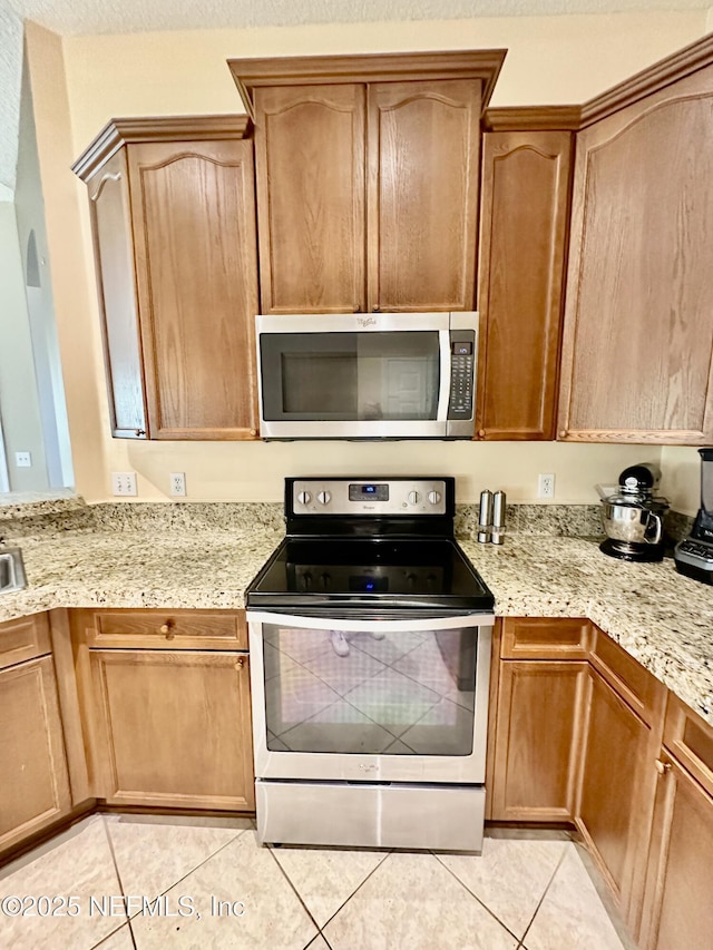 kitchen featuring light tile patterned floors, appliances with stainless steel finishes, a textured ceiling, and light stone countertops