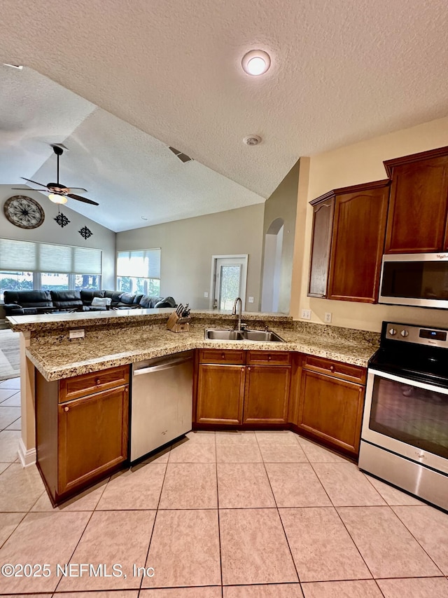 kitchen with appliances with stainless steel finishes, lofted ceiling, light tile patterned flooring, and a sink