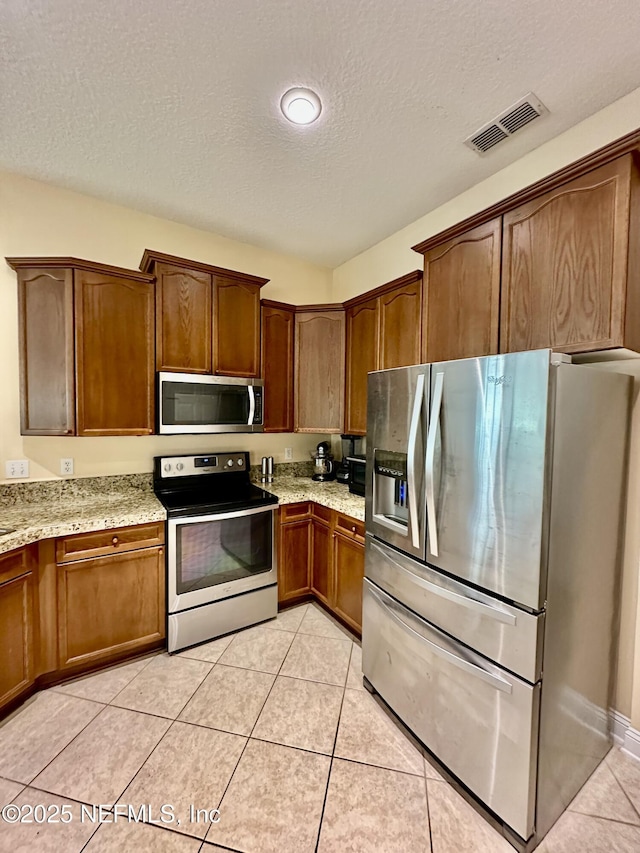 kitchen with visible vents, brown cabinetry, light stone counters, stainless steel appliances, and light tile patterned flooring