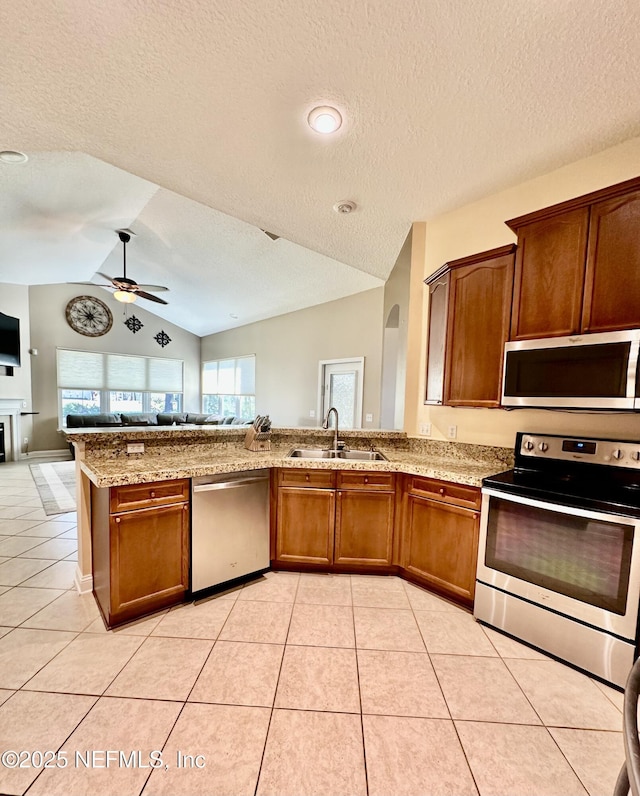 kitchen featuring stainless steel appliances, lofted ceiling, open floor plan, light tile patterned flooring, and a sink