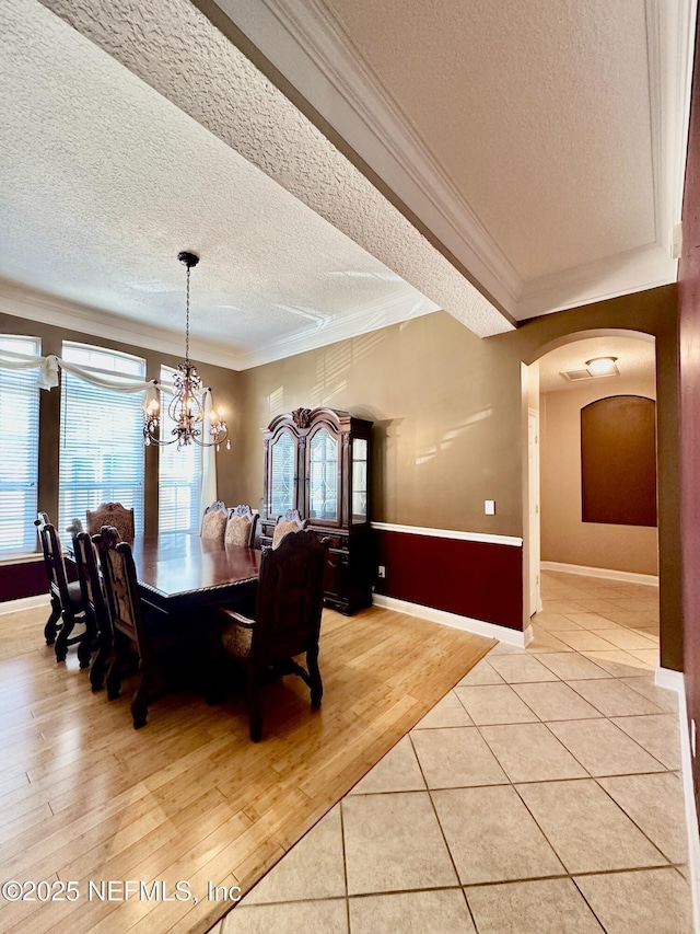 dining room with light wood finished floors, arched walkways, ornamental molding, an inviting chandelier, and a textured ceiling