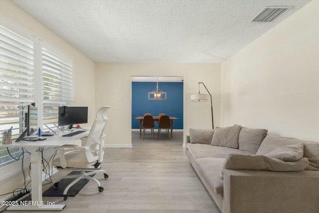 office space featuring light wood-style floors, baseboards, visible vents, and a textured ceiling