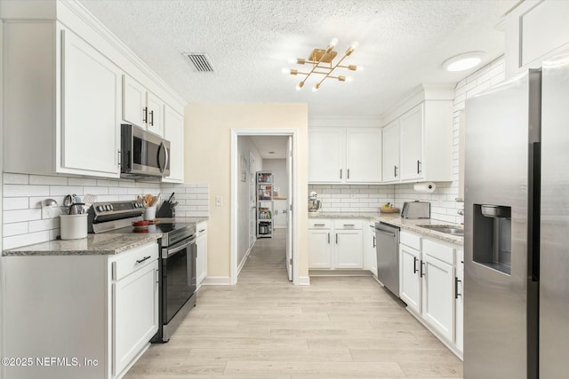 kitchen with appliances with stainless steel finishes, light wood-style flooring, visible vents, and white cabinets