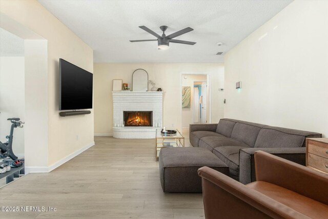 living area with a fireplace, visible vents, light wood-style floors, ceiling fan, and baseboards