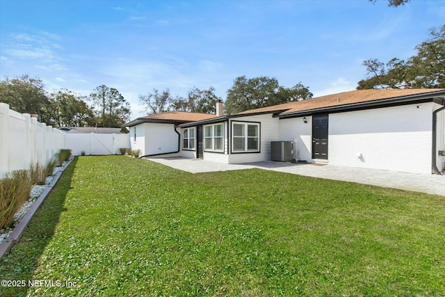 rear view of property featuring central AC unit, a lawn, a fenced backyard, a patio area, and brick siding