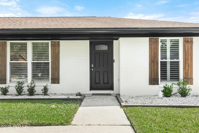 entrance to property with roof with shingles and brick siding