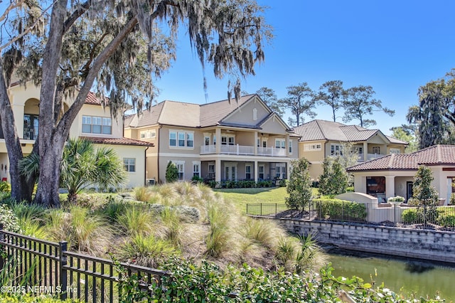 back of property featuring a water view, a tiled roof, fence, and stucco siding