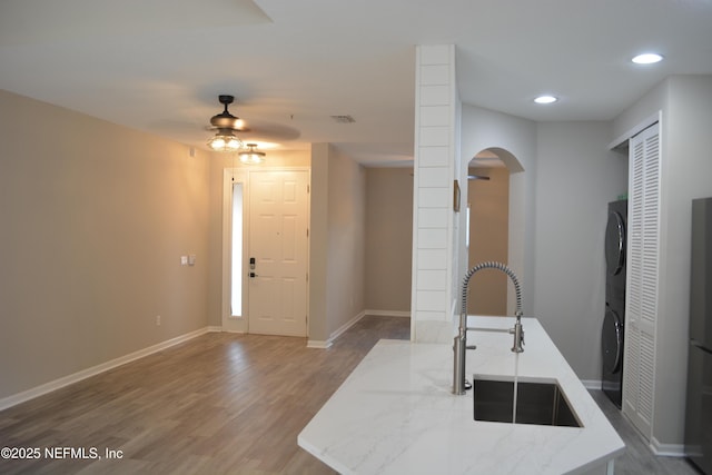 kitchen with baseboards, stacked washer and clothes dryer, light stone counters, wood finished floors, and a sink