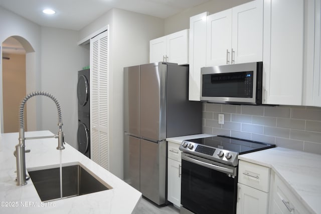 kitchen with stacked washer / dryer, a sink, appliances with stainless steel finishes, backsplash, and light stone countertops