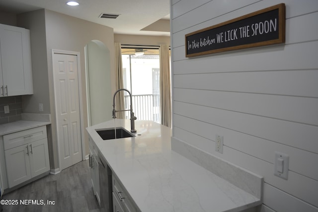 kitchen with visible vents, wood finished floors, a sink, light stone countertops, and backsplash