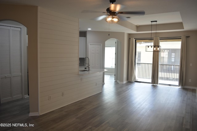 unfurnished living room with arched walkways, a tray ceiling, a sink, and dark wood finished floors