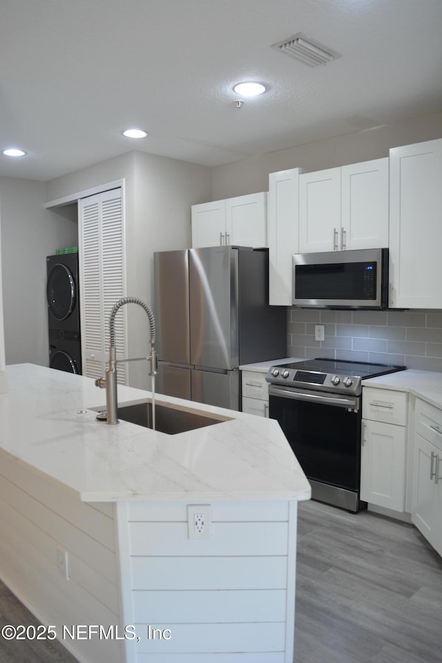 kitchen featuring a sink, visible vents, appliances with stainless steel finishes, stacked washing maching and dryer, and tasteful backsplash