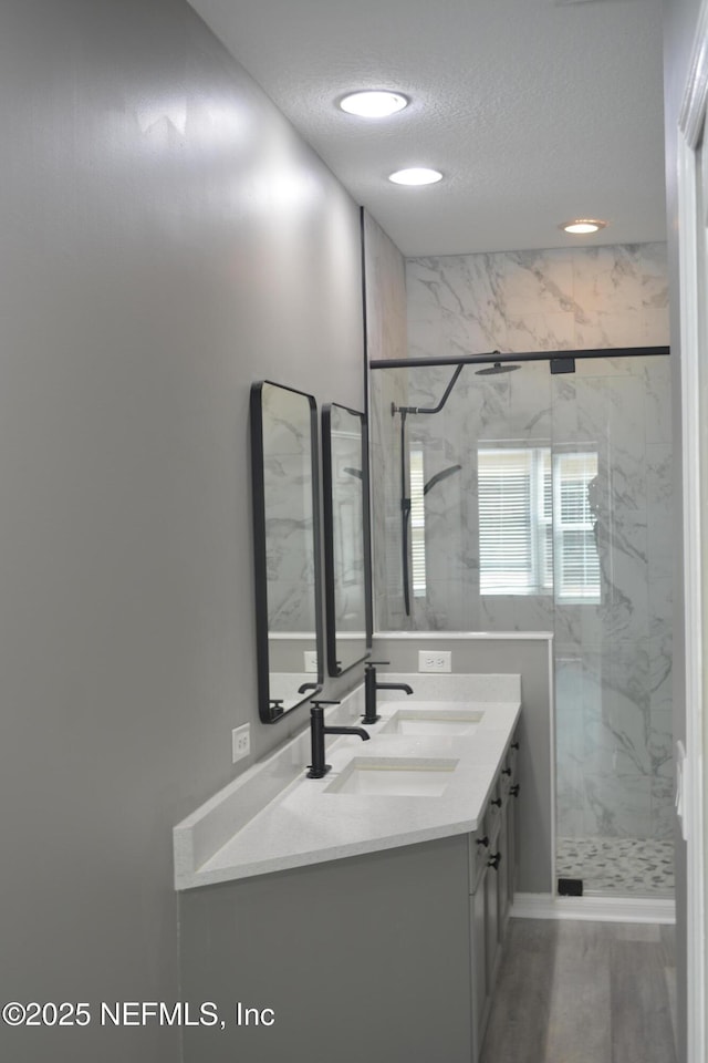 bathroom with a marble finish shower, wood finished floors, a textured ceiling, and vanity