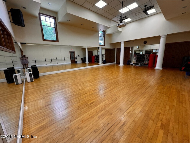 misc room featuring a drop ceiling, light wood-type flooring, decorative columns, and a towering ceiling