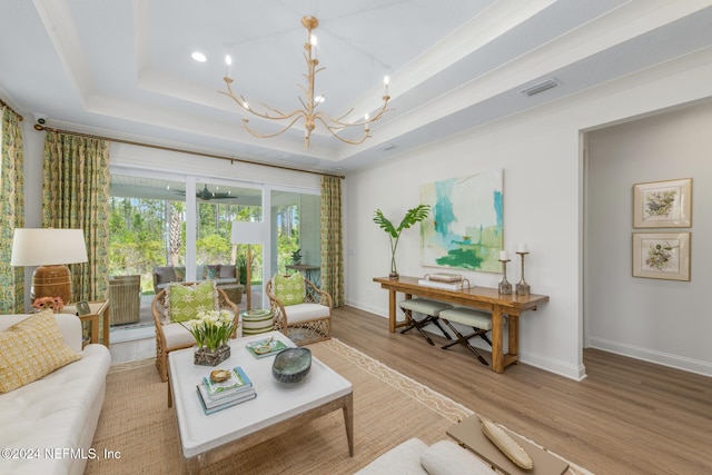 living area featuring a tray ceiling, a notable chandelier, visible vents, wood finished floors, and baseboards