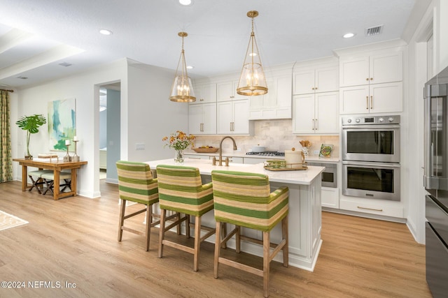 kitchen with tasteful backsplash, an island with sink, light wood-style flooring, appliances with stainless steel finishes, and light countertops