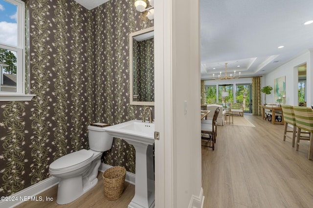 bathroom with toilet, wood finished floors, baseboards, a tray ceiling, and wallpapered walls