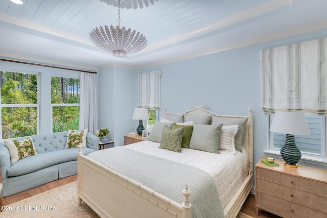 bedroom with light wood-style floors, a tray ceiling, and a chandelier