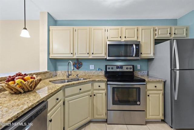 kitchen with light stone counters, stainless steel appliances, cream cabinetry, a sink, and light tile patterned flooring