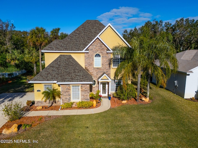 traditional home with stone siding, roof with shingles, a front lawn, and stucco siding