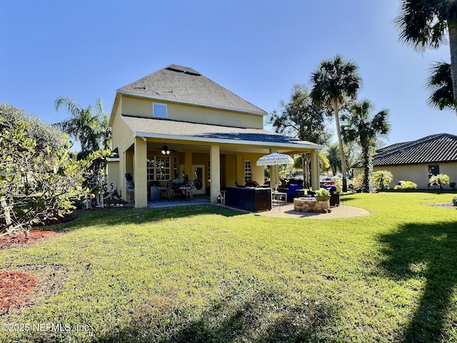 rear view of property with a patio area, ceiling fan, a lawn, and stucco siding