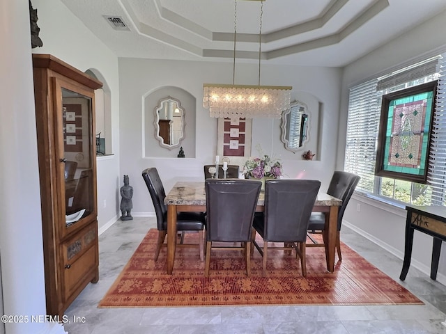 dining space with a tray ceiling, visible vents, and baseboards