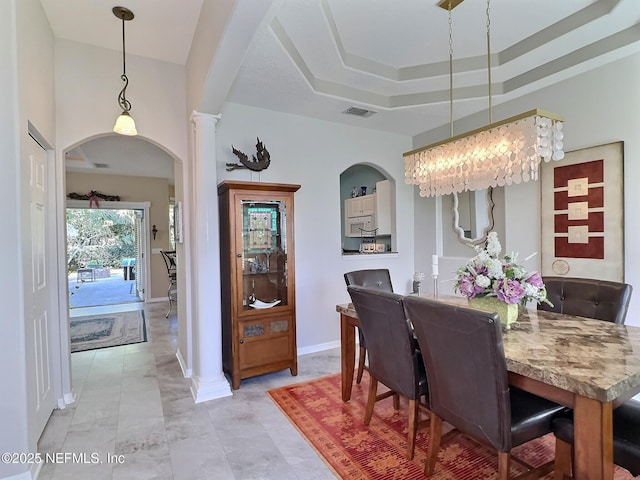 dining room featuring arched walkways, a raised ceiling, visible vents, ornate columns, and baseboards