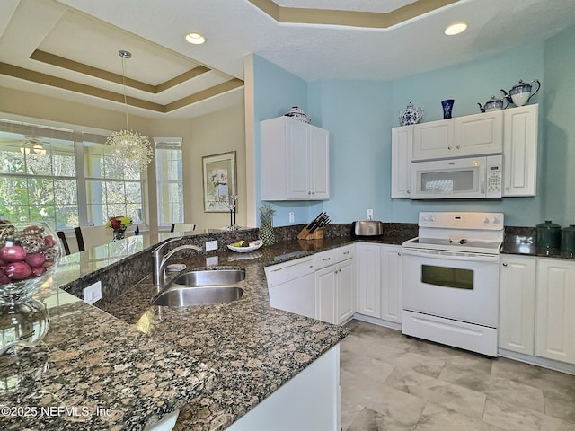 kitchen featuring white appliances, a sink, white cabinetry, a tray ceiling, and dark stone countertops