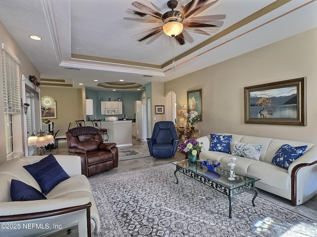 living area featuring a tray ceiling, arched walkways, a ceiling fan, and recessed lighting