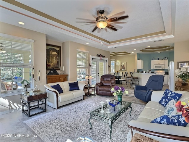 living area with a healthy amount of sunlight, a tray ceiling, and a ceiling fan