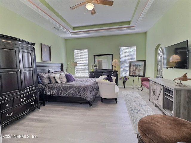 bedroom with arched walkways, ceiling fan, a raised ceiling, and light wood-style floors