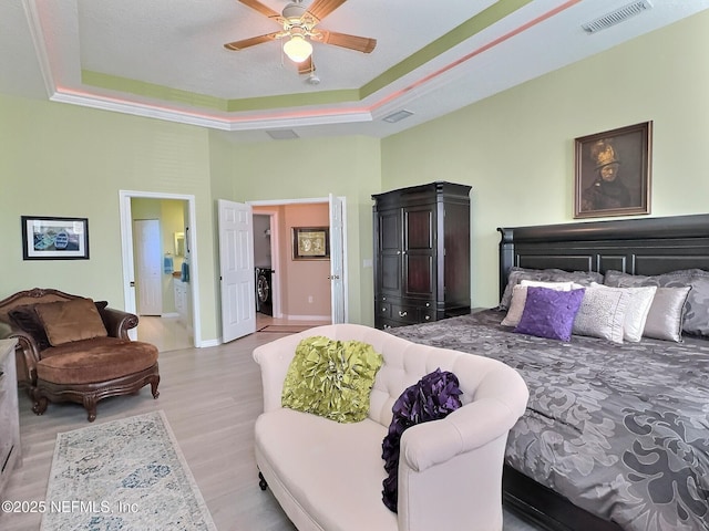 bedroom featuring washer / clothes dryer, light wood-type flooring, a raised ceiling, and visible vents