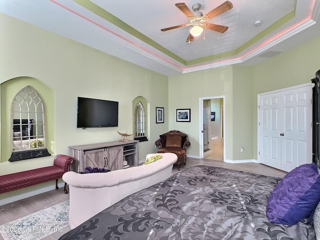 living area featuring baseboards, arched walkways, a ceiling fan, wood finished floors, and a tray ceiling